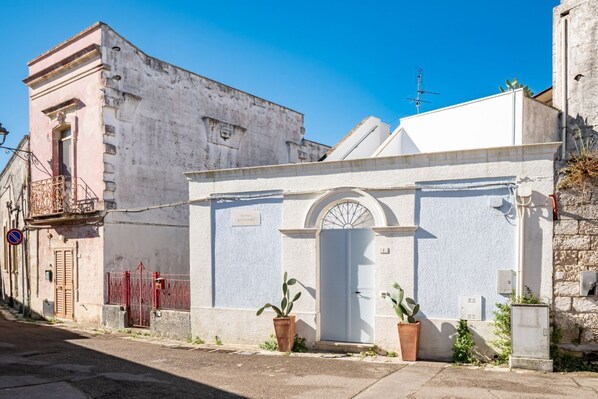 Ein Gebäude mit weißer Fassade, einer Tür mit Rundbogen und zwei Blumentöpfen davor.
