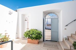 A white building with a blue door, a potted plant, a metal lamp, and a staircase.