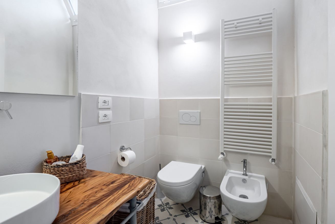 Un baño con tocador de madera, un lavamanos blanco, un inodoro, un bidé y un perchero para toallas.