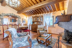 A cozy living room with a stone archway, wooden furniture, a fireplace, and a chandelier.