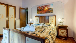 A bedroom with a wooden bed, a nightstand with a lamp, a painting of a sunset, and a wardrobe. - GuestHost - Wonderful 140 sqm apartment, perfect for 7 people, located on the first floor of an old renovated semi-detached house surrounded by greenery (stairs to access it).The apartment is located in Borgo a Mozzano, a picturesque village immersed in  (Borgo a Mozzano)