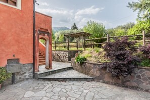 A stone staircase leading to a wooden door, a stone wall with plants, and a view of greenery and hills in the background.