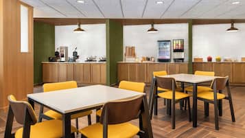 Un espace repas avec des tables en bois et des chaises jaunes, un comptoir avec une machine à café et un réfrigérateur.