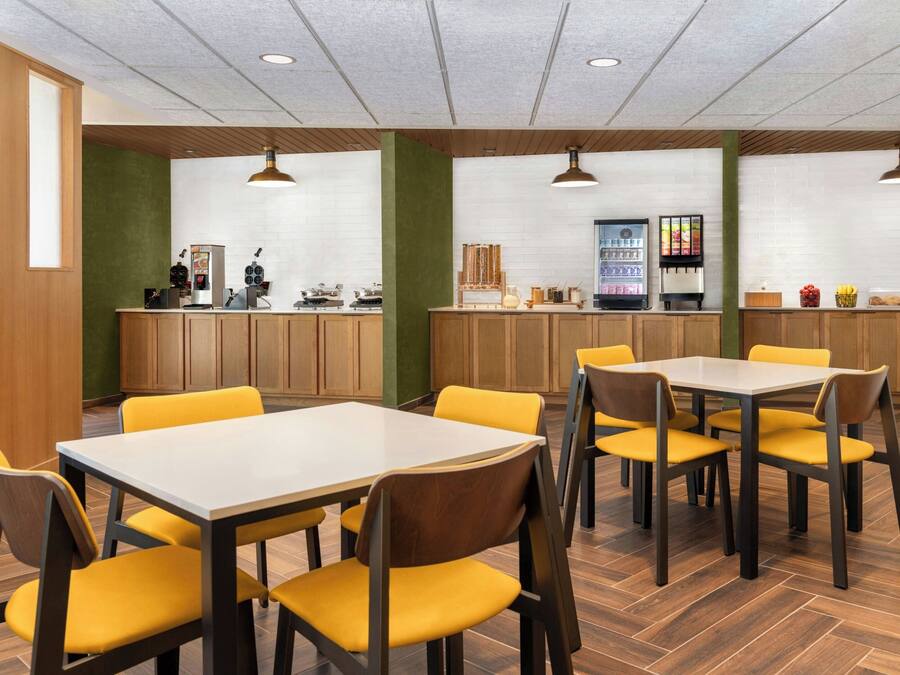 Un espace repas avec des tables en bois et des chaises jaunes, un comptoir avec une machine à café et un réfrigérateur.