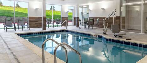 An indoor swimming pool with a clear view of the outdoors, including a grassy hill.