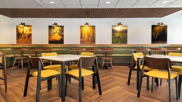 A restaurant with wooden flooring, yellow cushioned chairs, and a long bench.