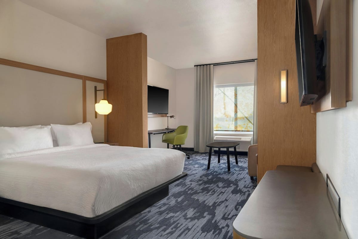 A hotel room with a large bed, a desk, a chair, a small table, and a TV mounted on the wall.