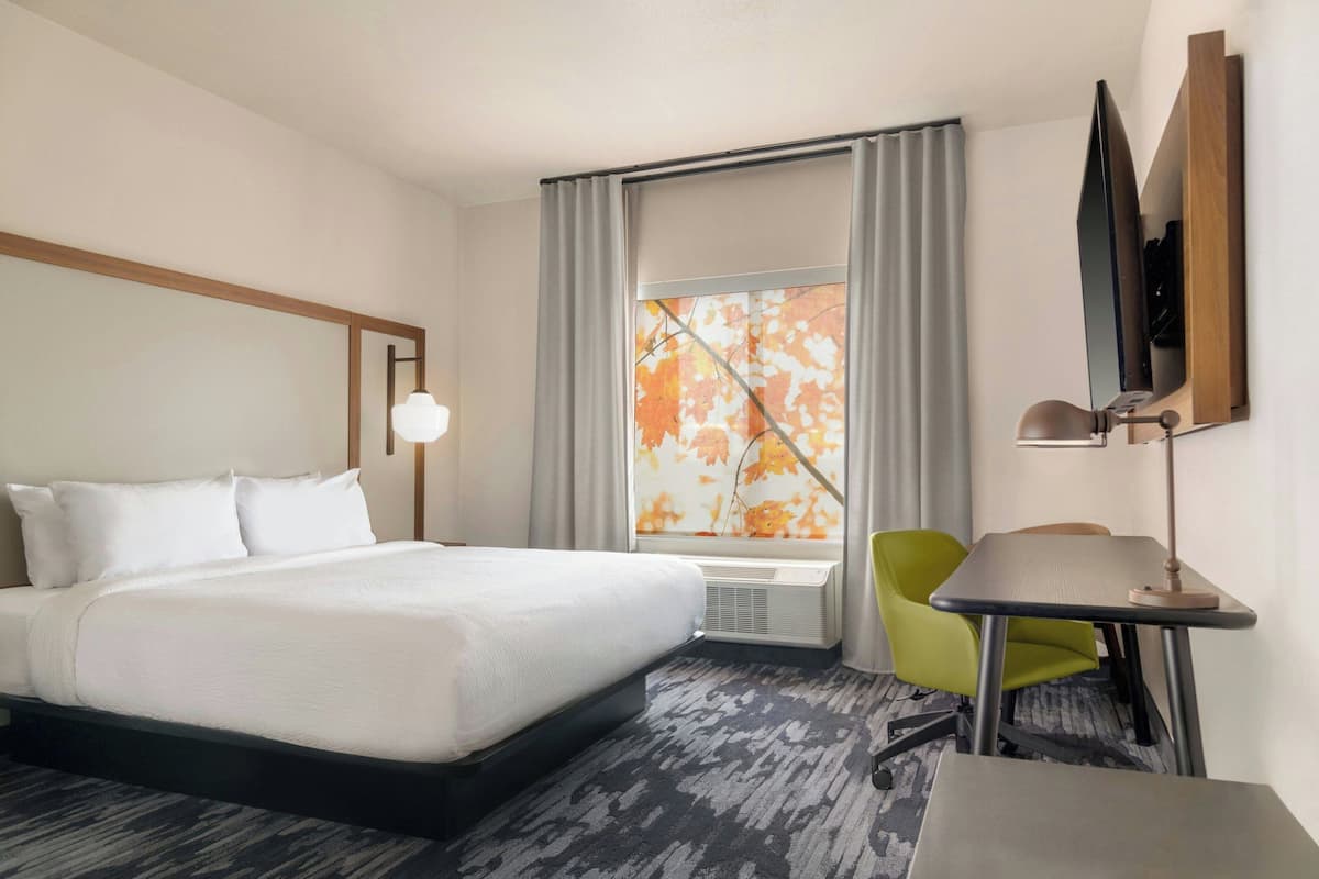 A hotel room with a bed, a desk, a chair, a TV, and a window with curtains.