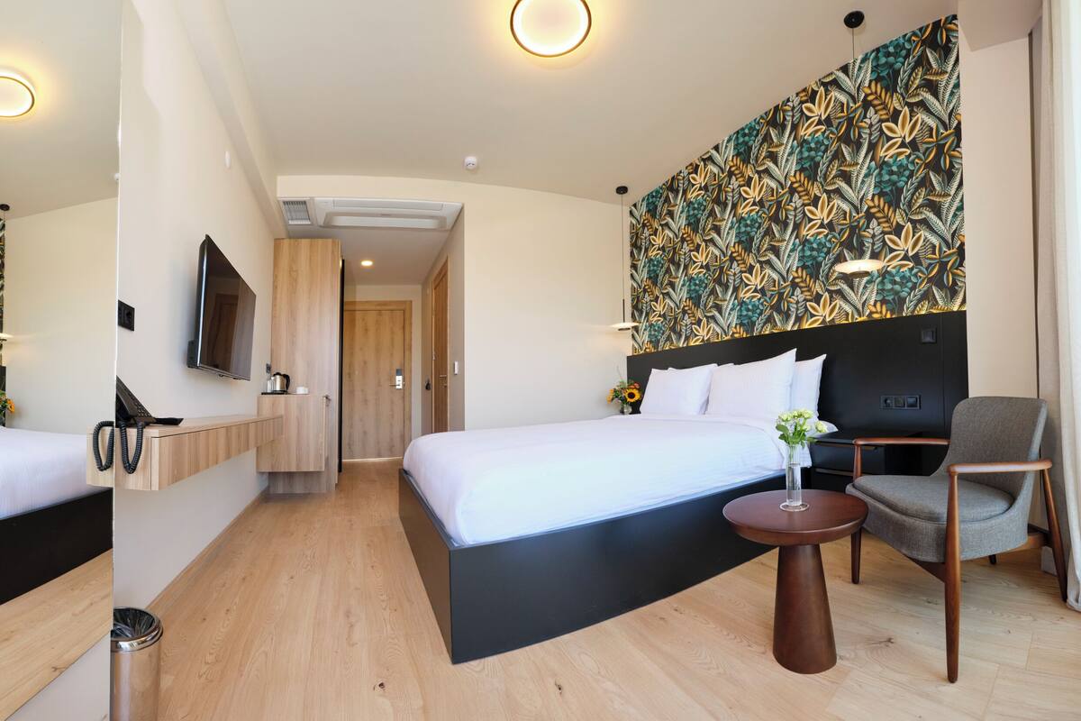 Une chambre d’hôtel moderne équipée d’un grand lit, d’un bureau, d’une chaise et d’un téléviseur fixé au mur.