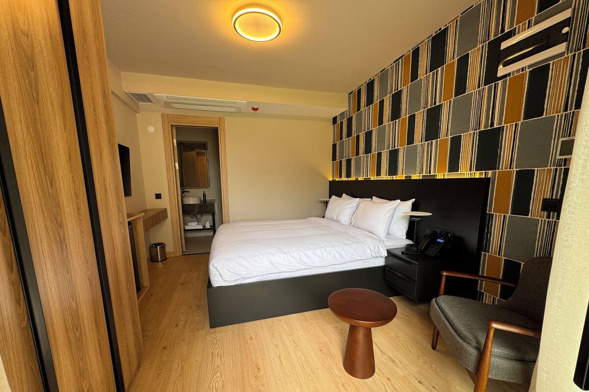 Une chambre d’hôtel moderne avec un grand lit, une table de chevet, une chaise et un mur décoré d’un motif original.