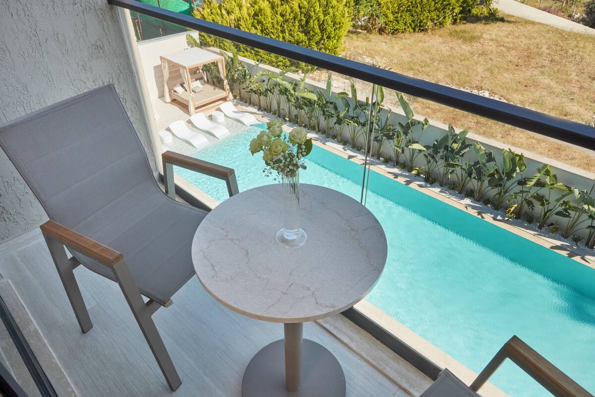 Un balcon avec une piscine, des chaises longues et une table agrémentée d’un vase de fleurs.