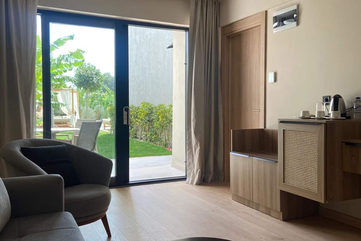 Une chambre d’hôtel moderne, dotée d’un canapé, d’une table ronde, d’un meuble en bois et d’une porte-fenêtre coulissante donnant sur un balcon.
