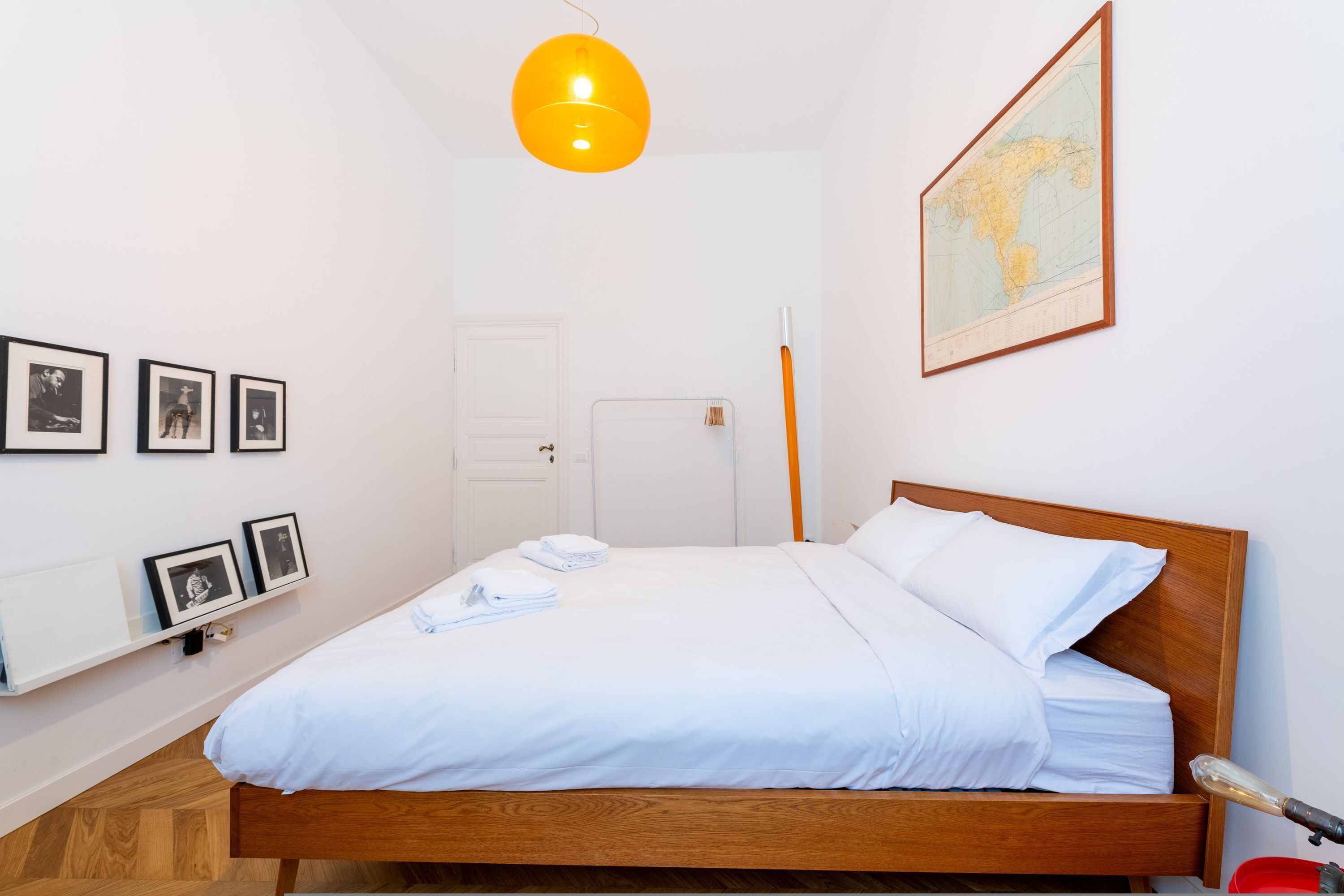 A neatly made bed with white linens, a wooden headboard, and a map on the wall.