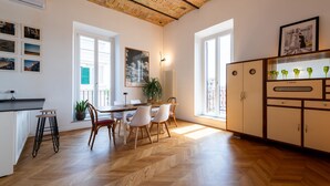 A modern kitchen with a herringbone wood floor, white cabinetry, and a dining area with a wooden table and chairs.