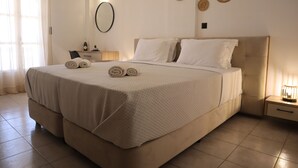 Un lit bien fait, avec une tête de lit beige et du linge de lit blanc, une table de chevet avec une lampe et un miroir fixé au mur.