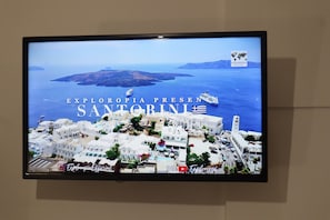 A television screen displaying a view of Santorini with the text "EXLORPIA PRESENTS SANTORINI". - pension st.george (Santorini)