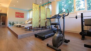 Een fitnessruimte met trainingsapparatuur, een loopband en een hometrainer.