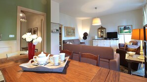 Een woonkamer met een eettafel gedekt voor thee, een bank en een televisie.