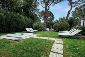 Un jardin avec un jacuzzi, deux chaises longues et un chemin en pierre.