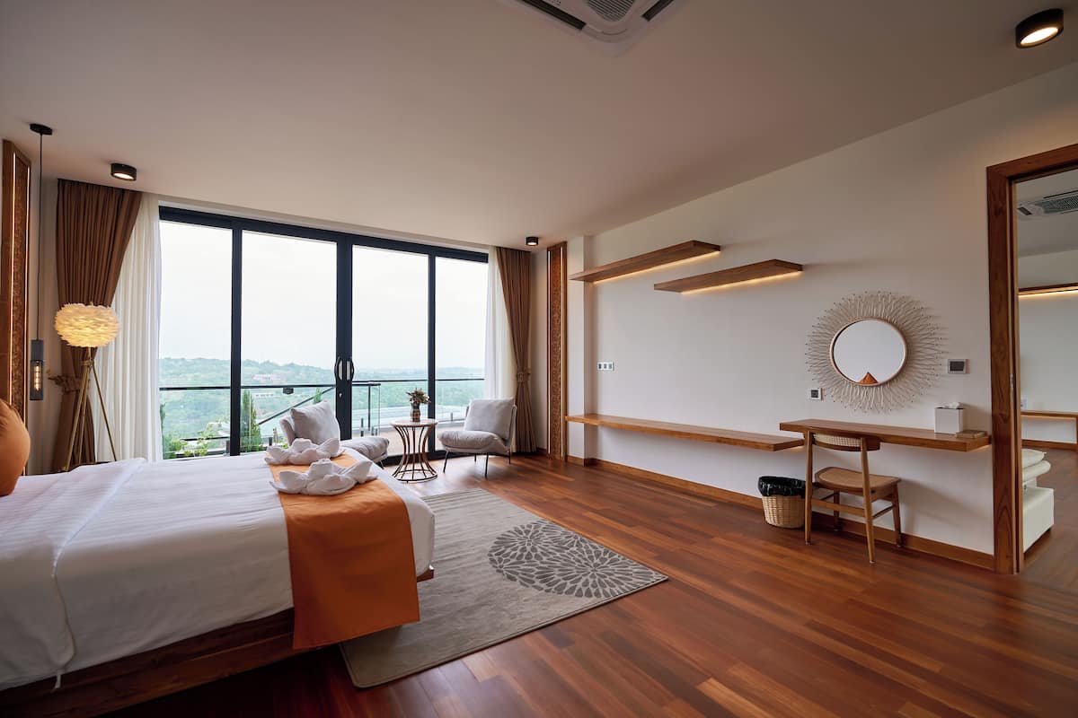 A modern hotel room with a large bed, a desk, and a view of the outdoors.