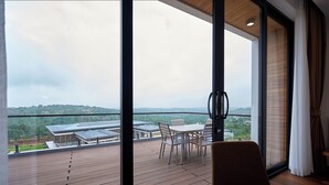A balcony with a table and chairs, overlooking a building and greenery. - The Pine Mansion (Sen Monorom)