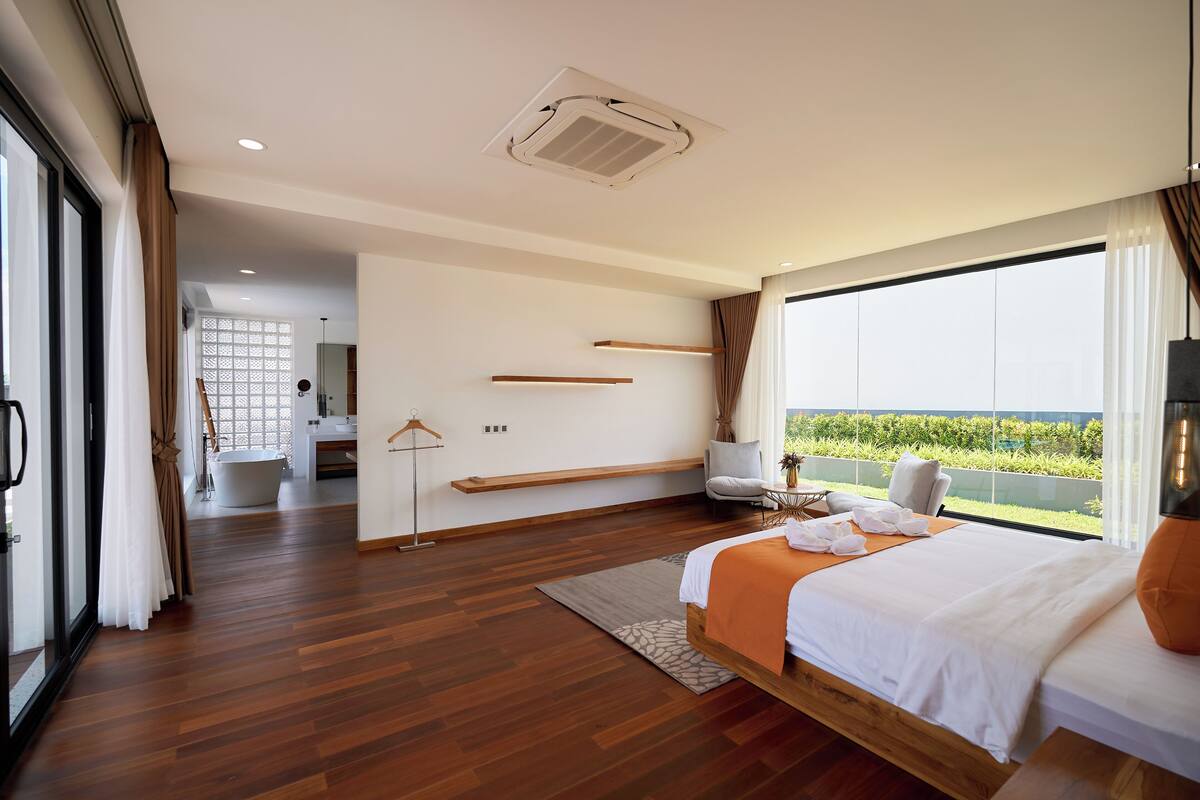 A modern hotel room with a large bed, a view of the outdoors, a bathroom, and a seating area.
