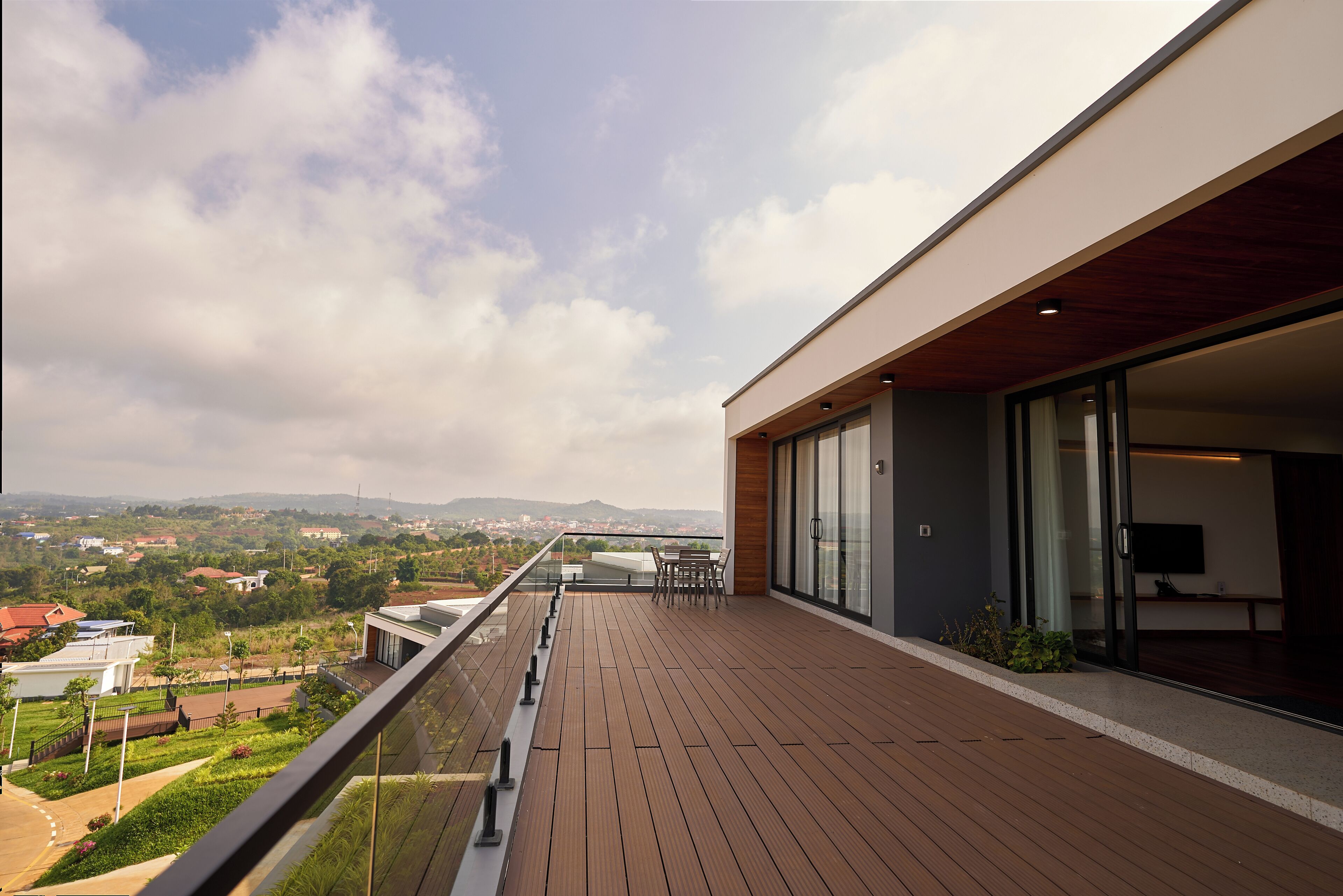 A modern balcony with a wooden floor, glass doors, and a view of a cityscape.
