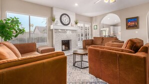 A modern living room with a fireplace, leather sofas, and a large window. - Solstice on Summit Retreat|Pool|Putt Grn|Sleeps 10 (Chandler)