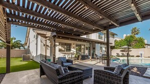 An outdoor patio with wicker furniture, a pool, and a covered area with a pergola. - Solstice on Summit Retreat|Pool|Putt Grn|Sleeps 10 (Chandler)