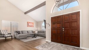 A spacious living room with a large wooden door, a gray sectional sofa, a coffee table, and a patterned rug. - Solstice on Summit Retreat|Pool|Putt Grn|Sleeps 10 (Chandler)