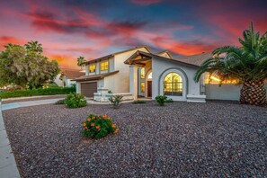Una casa moderna con entrada para vehículos, un césped cuidado y un cielo al atardecer.