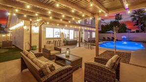 An outdoor patio area with wicker furniture, string lights, and a pool. - Solstice on Summit Retreat|Pool|Putt Grn|Sleeps 10 (Chandler)