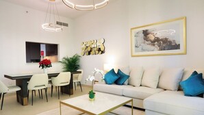 A modern living room with a sofa, coffee table, dining area, and artwork. - 2BR Stylish Corner Unit with Dubai Mall Access (Dubai)