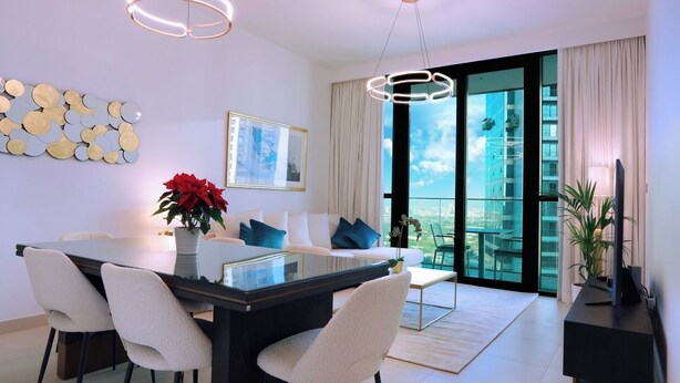 A modern living room with a glass dining table, white sofas, and a large window with a city view. - 2BR Stylish Corner Unit with Dubai Mall Access (Dubai)