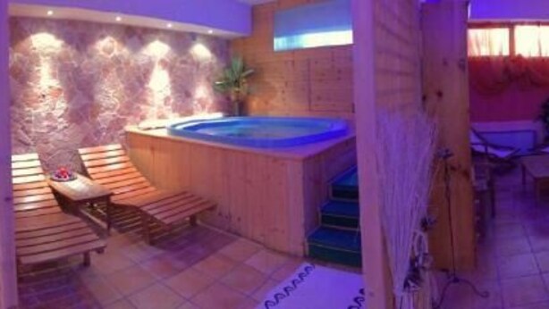 A spa area with a hot tub, wooden seating, and a stone wall. - ALBA SPORTING HOTEL (Rocca di Mezzo)