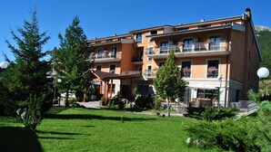 A multi-story hotel with balconies, a covered outdoor area, and a well-maintained lawn. - ALBA SPORTING HOTEL (Rocca di Mezzo)