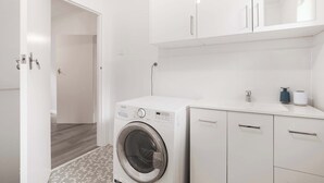 Moderni pyykinhuone, jossa on etuaukollinen pesukone, valkoiset kaapit ja laatoitettu lattia.