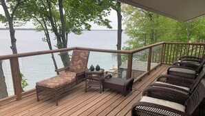A wooden deck with wicker furniture, a glass railing, and a view of a lake.