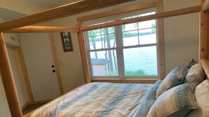 A bedroom with a large window, wooden beams, a bed with striped bedding, and a door with a picture on it.