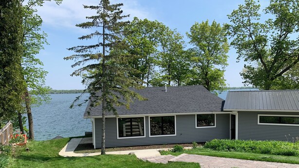 A modern house with a grey exterior, a paved driveway, and a view of a lake.
