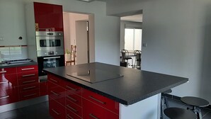 A modern kitchen with red cabinetry, a large island, and stainless steel appliances. - Location Villa Avec 2 Appartements Ind, Proche du Lac de Ste Croix et du Verdon (Régusse)