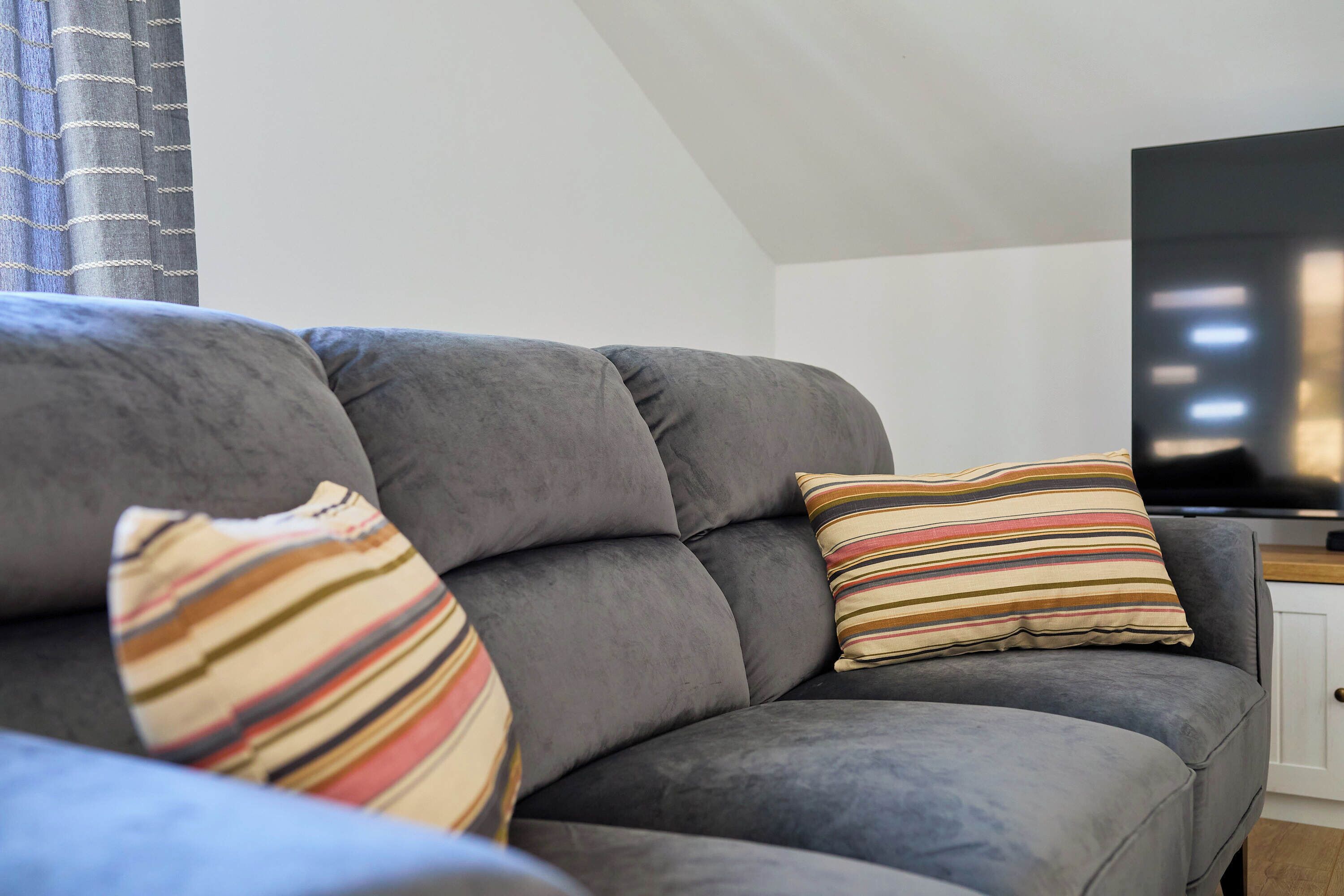 A grey sofa with striped pillows and a flat-screen TV in a modern living room.