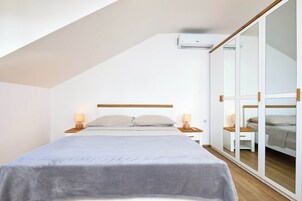 Un dormitorio moderno con techo inclinado, una cama con colcha gris, lámparas de noche y un mueble espejo grande.