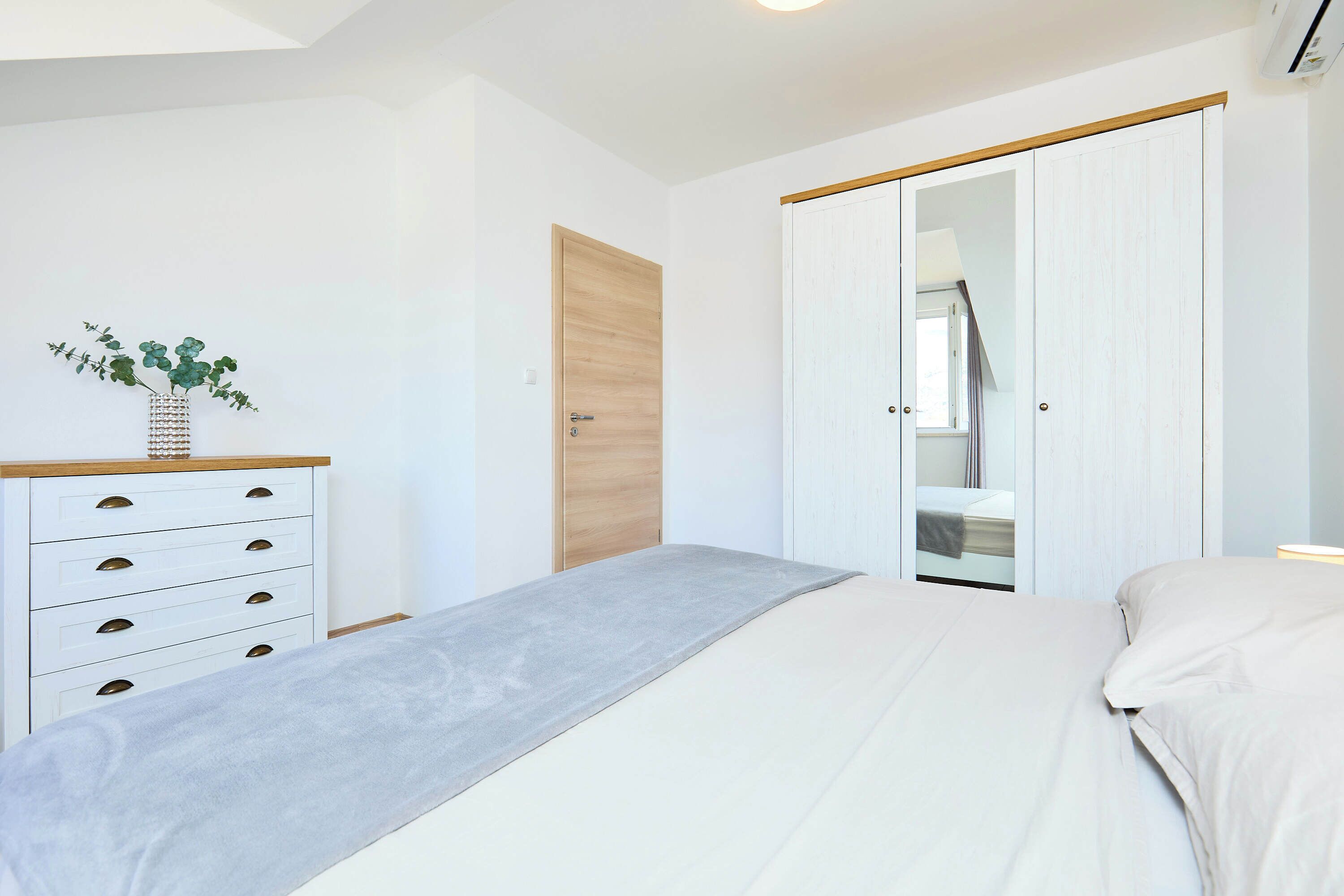 A bedroom with a bed, a dresser, a mirror, and a wardrobe.