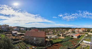 Un pueblo rural con edificios de piedra, jardines en terrazas y un cielo azul despejado.
