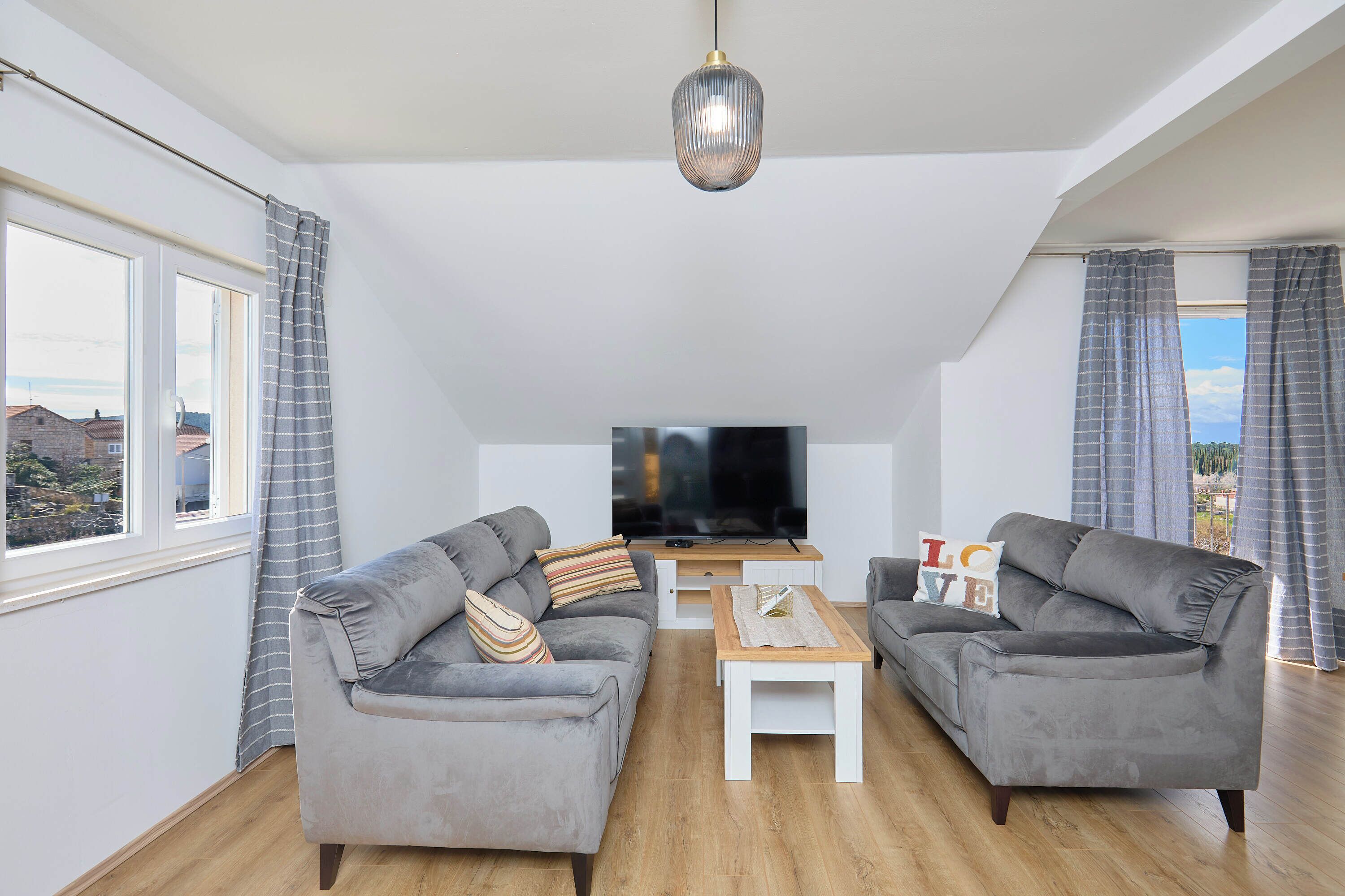 Un salon moderne avec deux canapés gris, une table basse en bois et un téléviseur à écran plat posé sur un meuble blanc.