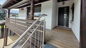 A wooden deck with a metal railing, a covered area with a door, and a view of the outside. - Neu Renovierte Ferienwohnung, 50qm, mit Vollausgestatteter Küche (Eggstätt)