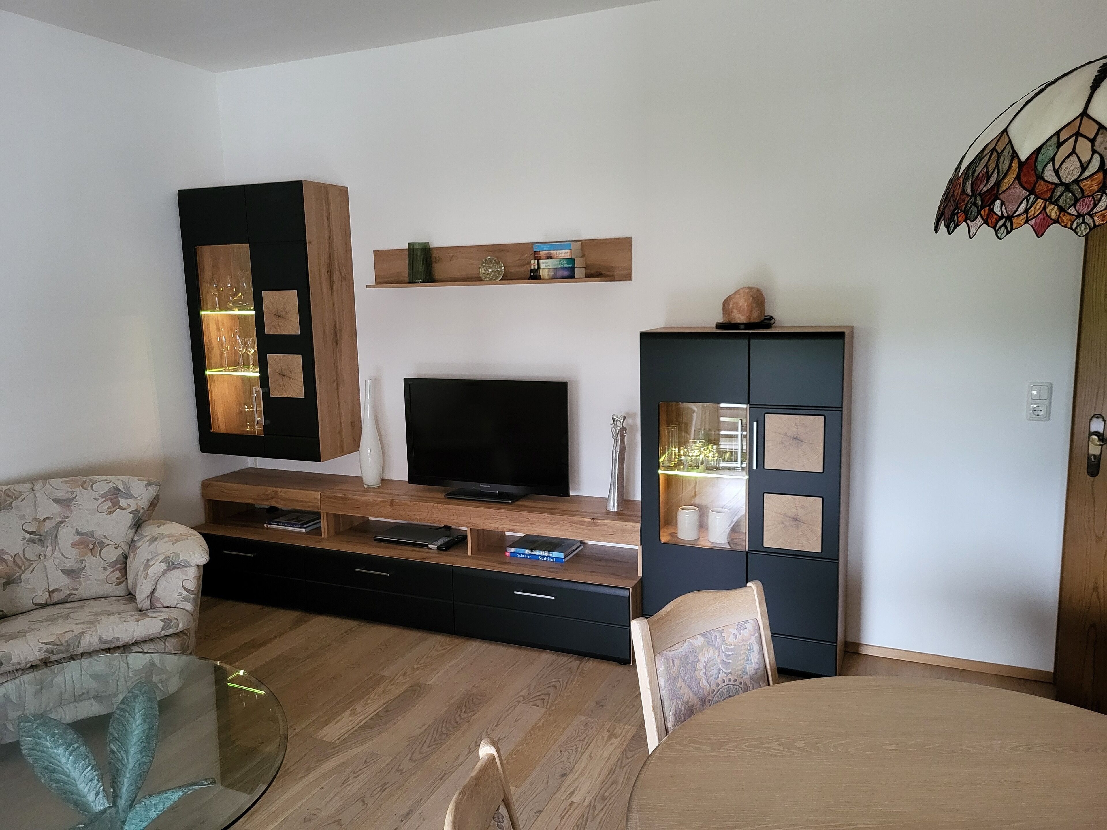 A modern living room with a flat-screen TV, wooden furniture, and a glass coffee table.