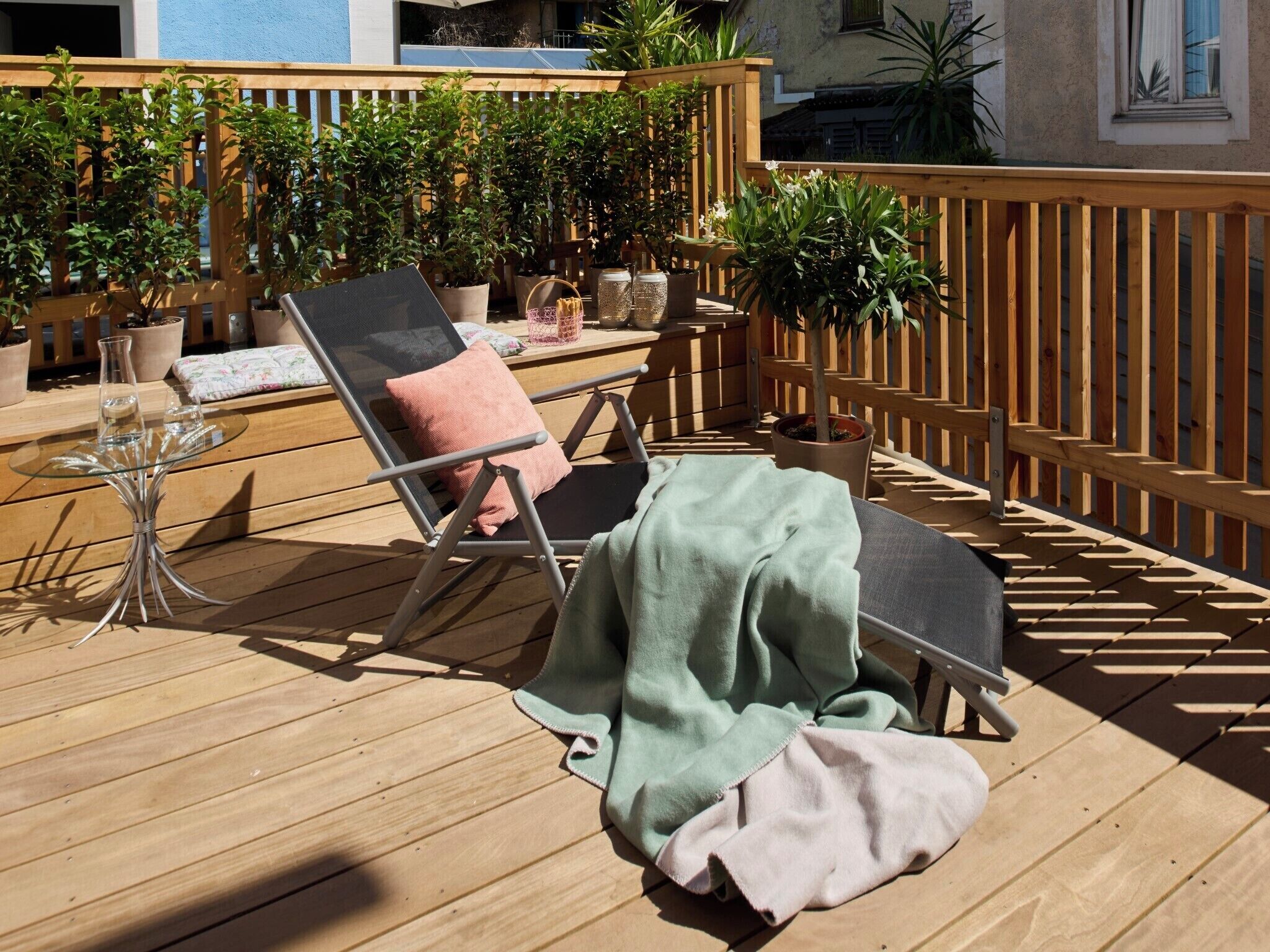 Une terrasse en bois avec un fauteuil de relaxation, une table en verre et des plantes en pot.
