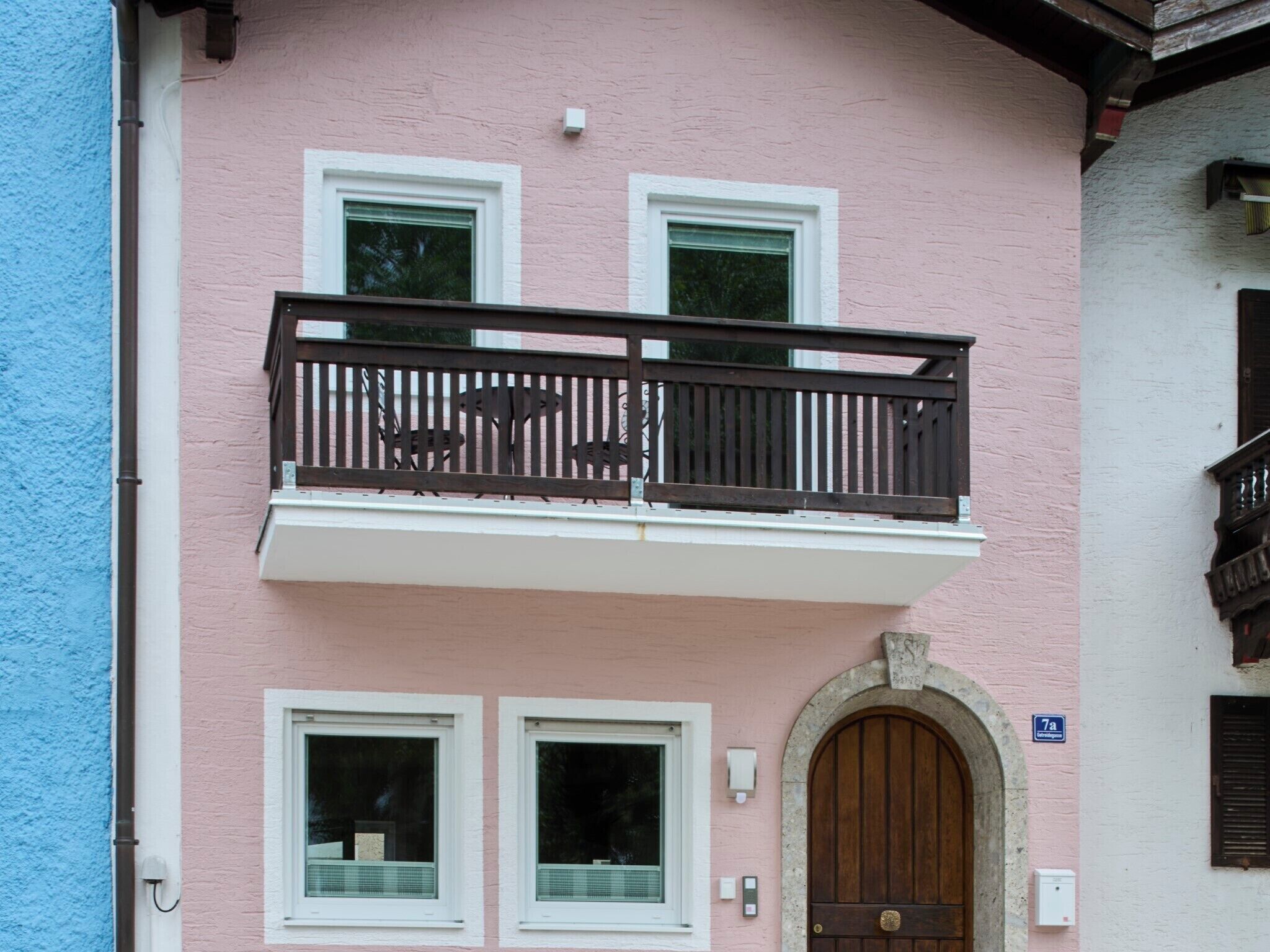 A pink building with a balcony, two windows, and a door.